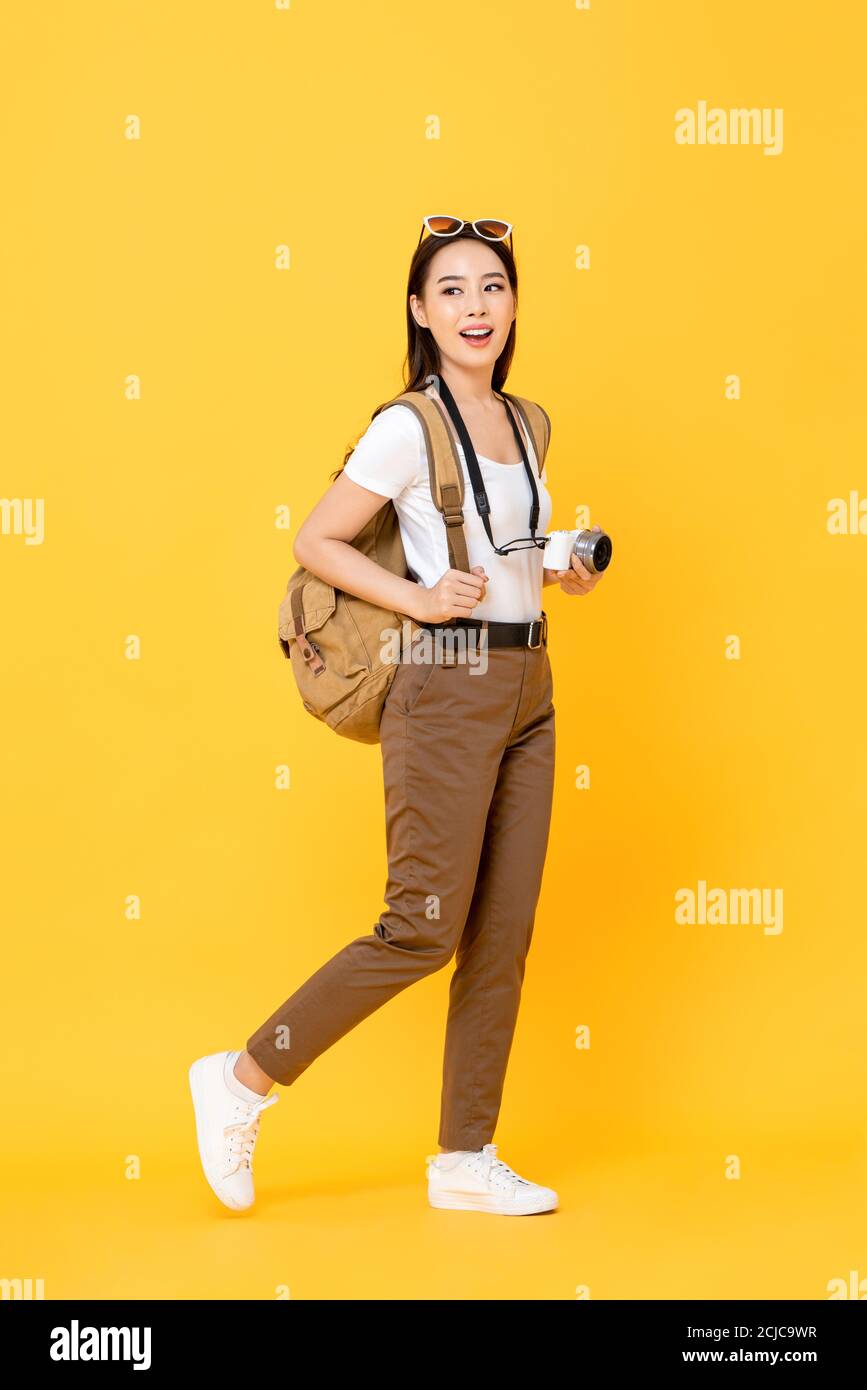 Ritratto a lunghezza intera di sorridente carino giovane turista asiatico con telecamera che cammina su isolato sfondo giallo studio Foto Stock