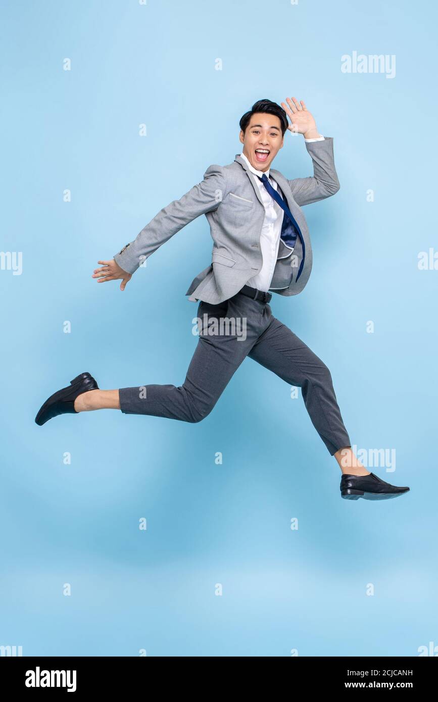 Ritratto divertente a lunghezza intera di felice giovane ed energico uomo d'affari asiatico salto in aria media isolato su sfondo blu studio Foto Stock