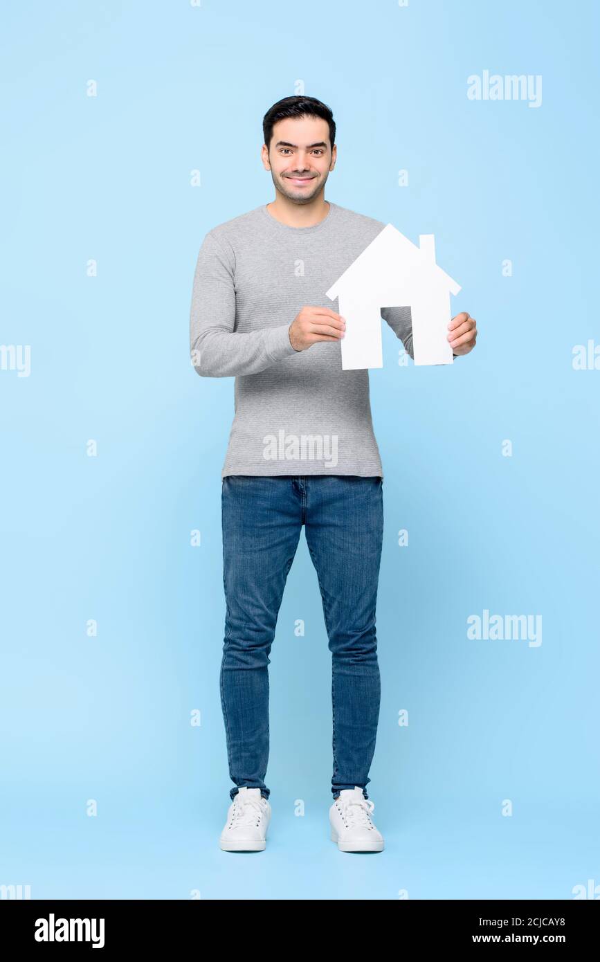 Ritratto a lunghezza intera di sorridente allegro uomo caucasico che tiene la casa modello ritagliato in uno sfondo di studio isolato blu chiaro Foto Stock