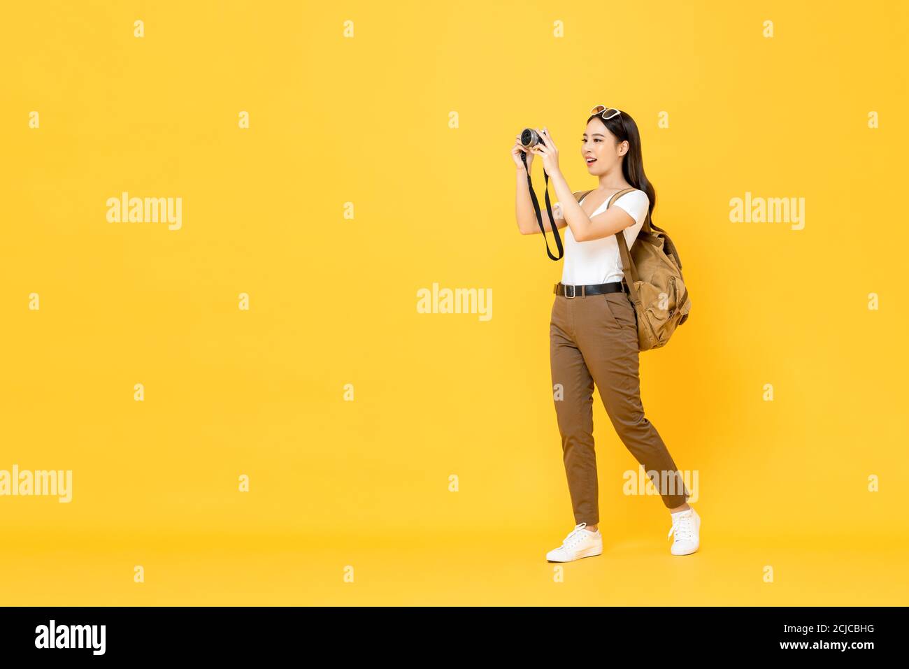 Giovane donna turistica asiatica che scatta foto con la fotocamera isolata sfondo giallo Foto Stock