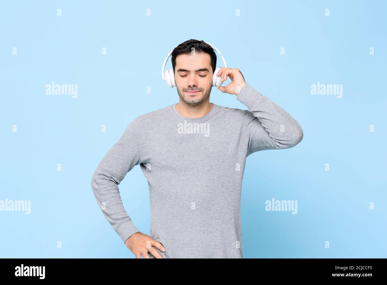 Vita in su ritratto di sorridente giovane bel caucasico che tiene cuffie e ascolto di musica in uno sfondo blu isolato Foto Stock