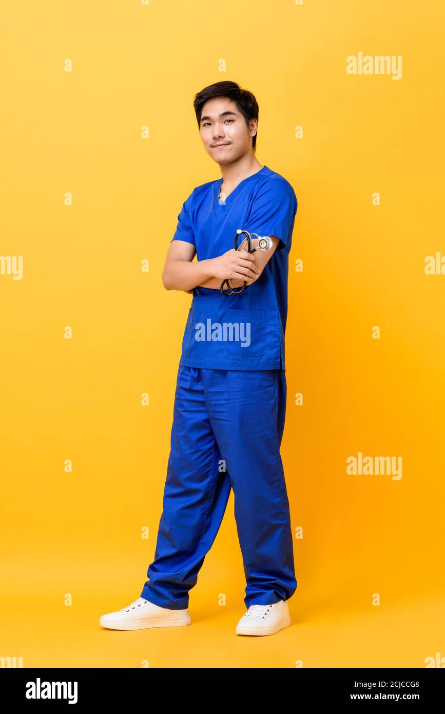 Ritratto a lunghezza intera di giovane infermiera asiatica sorridente con armi incrociate che tengono stetoscopio in studio isolato sfondo giallo Foto Stock