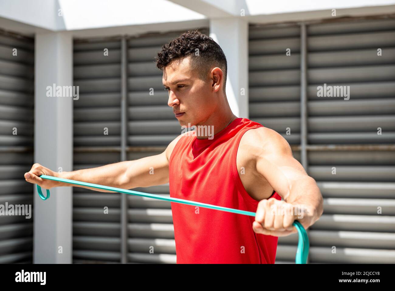 Bell'sportivo caucasico che fa esercizio di spalla con la banda di resistenza dentro tetto all'aperto Foto Stock