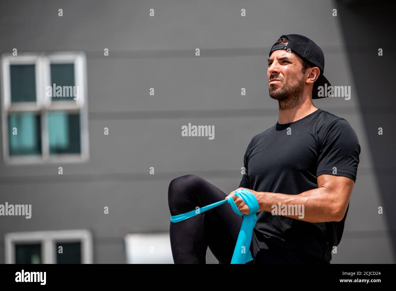 Montare sportivo caucasico facendo esercizio alle gambe con fascia di resistenza in tetto all'aperto Foto Stock