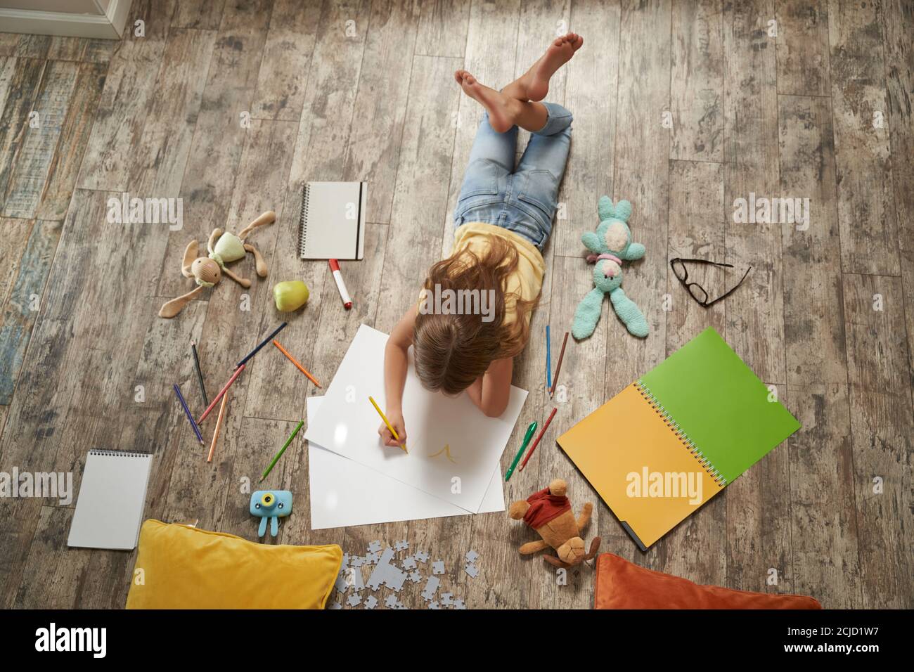 Hobby creativi per i bambini. Vista dall'alto della bambina caucasica sdraiata sul pavimento di legno a casa e disegnando con matite colorate su un foglio bianco di Foto Stock