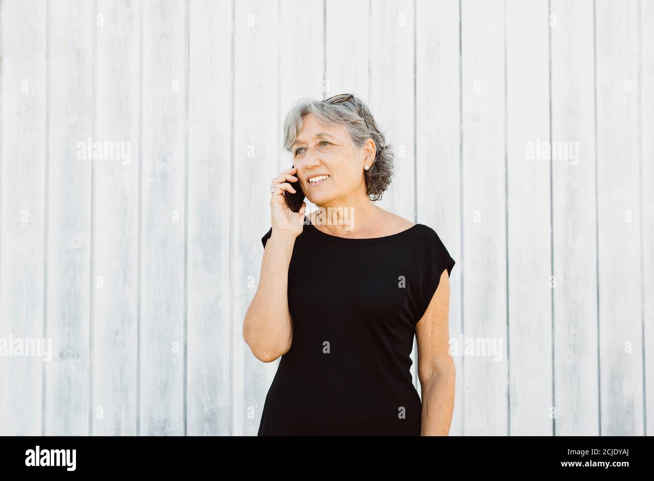 Donna anziana che parla su un telefono su un legno bianco background Foto Stock