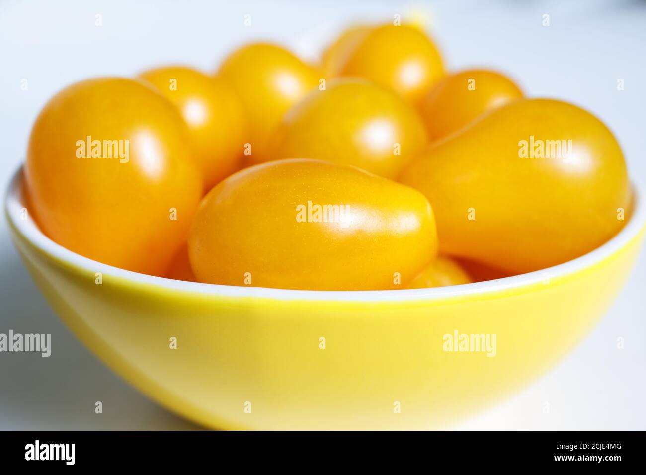 I pomodori ciliegini giallognolo si trovano in una ciotola gialla. Collezione autunnale di verdure. Raccolto brillante Foto Stock