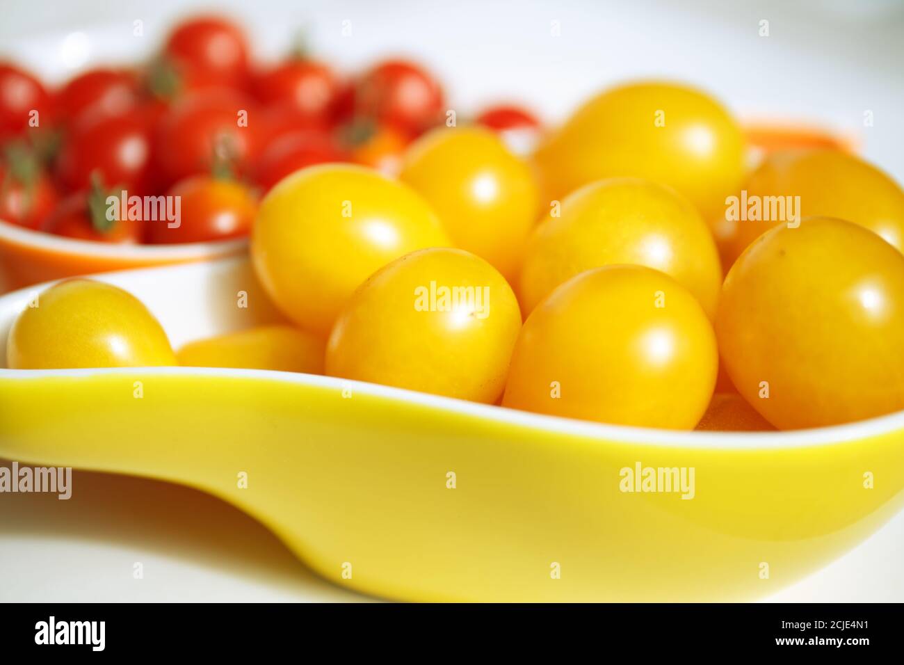 Pomodori ciliegini gialli e rossi. I pomodori ciliegini gialle si trovano in una ciotola gialla contro uno sfondo sfocato di piccoli pomodori rossi. Collezione autunnale di ve Foto Stock
