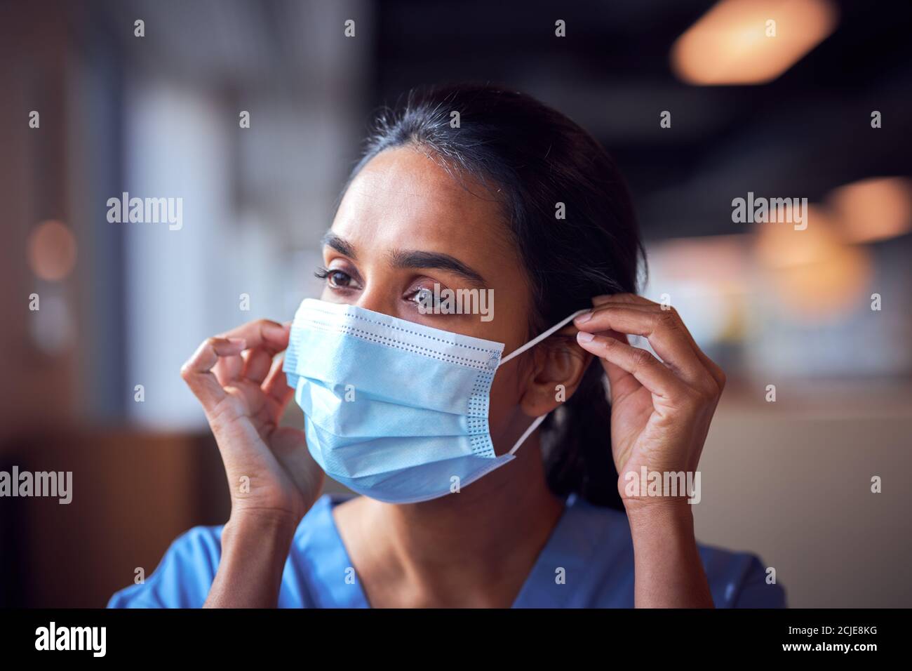 Dottore femminile in scrub mettendo su maschera di faccia sotto pressione In ospedale occupato durante Pandemic di salute Foto Stock