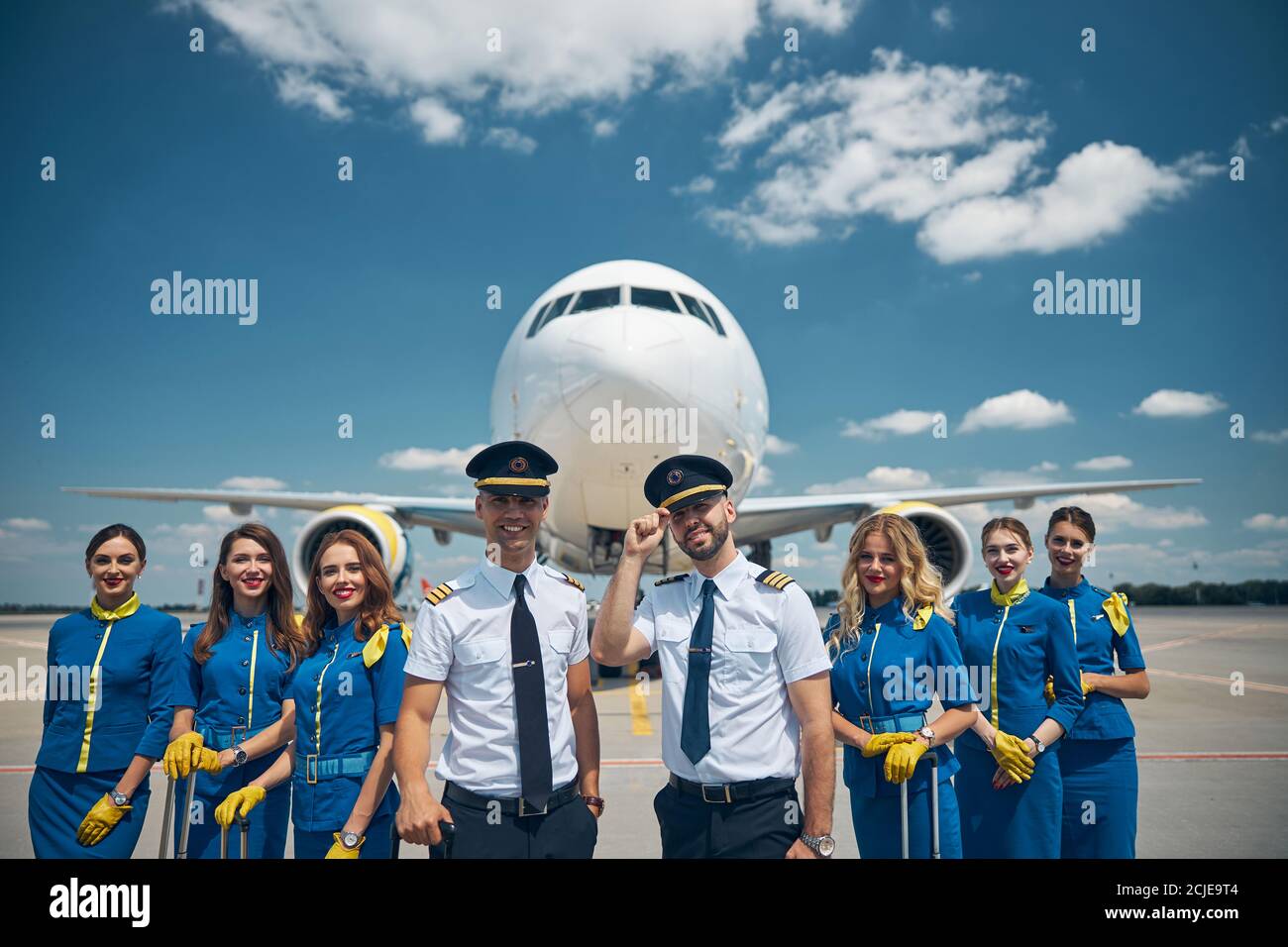 Allegri lavoratori delle compagnie aeree in piedi in campo aereo sotto il cielo blu Foto Stock