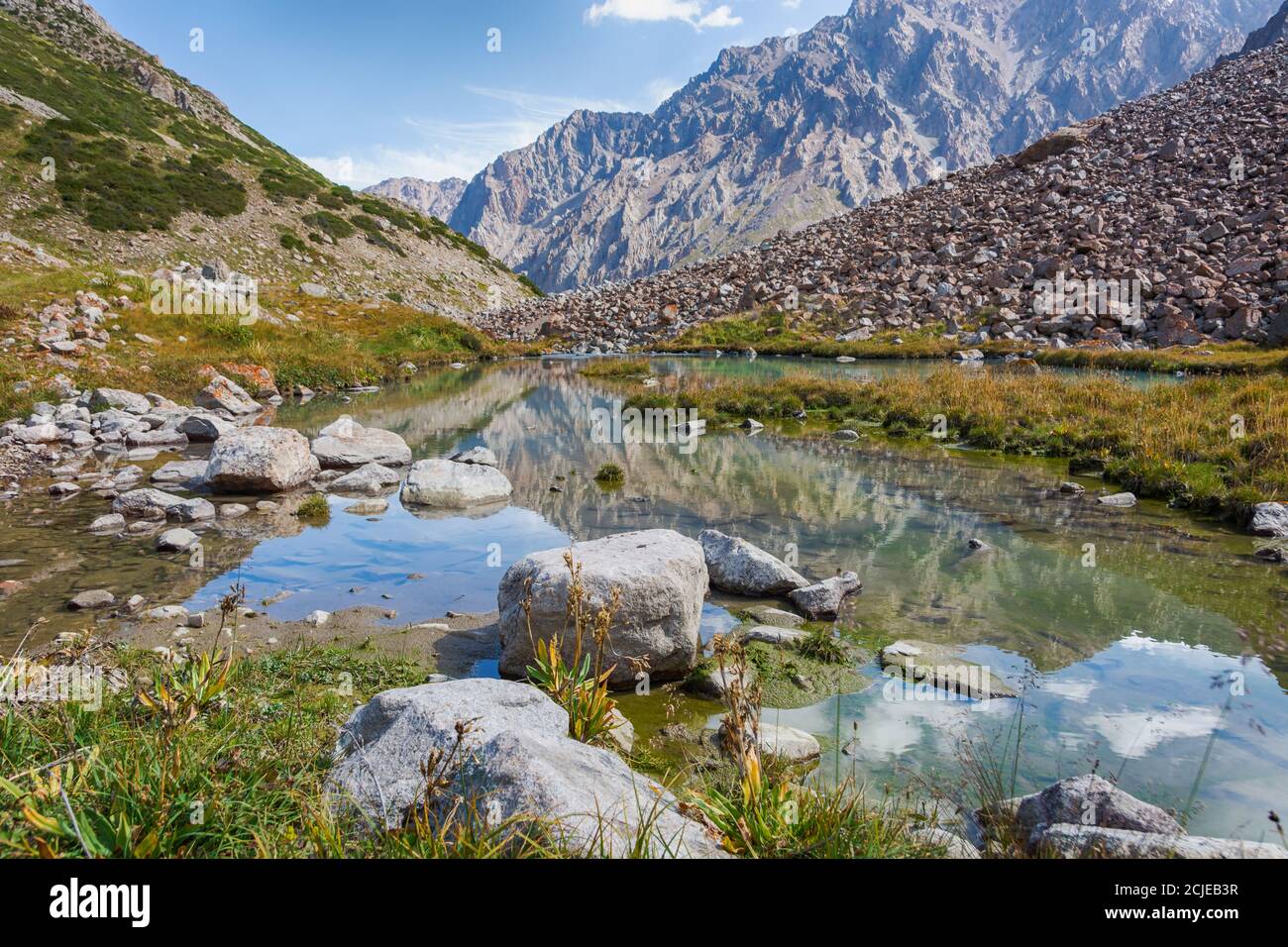 Idilliaco paesaggio estivo con sentieri escursionistici in montagna con bellissimi prati freschi di montagna, fiume con riflessi e nuvole. Foto Stock