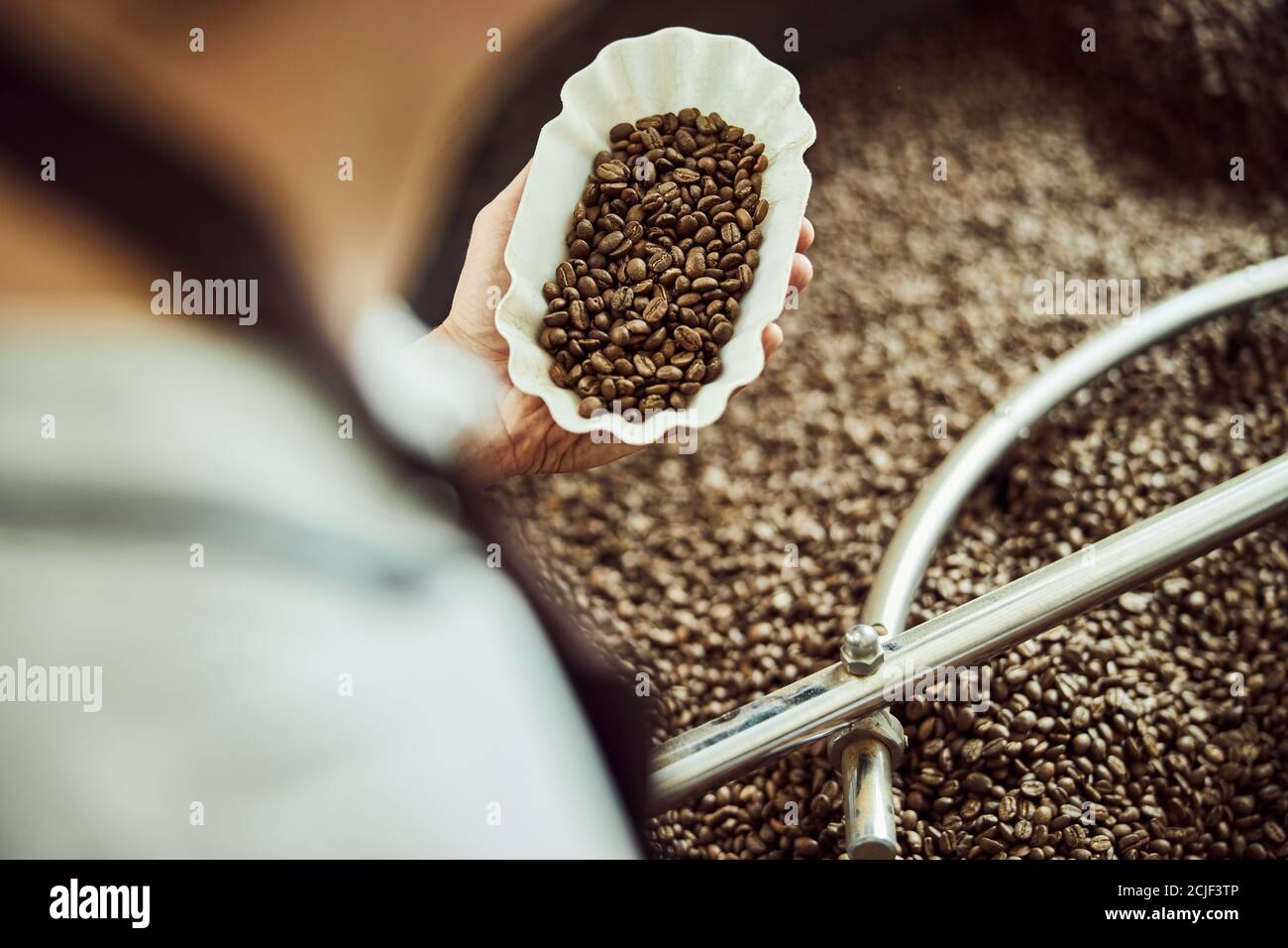 Lavoratore maschile che tiene in mano la ciotola di chicchi di caffè appena tostati Foto Stock