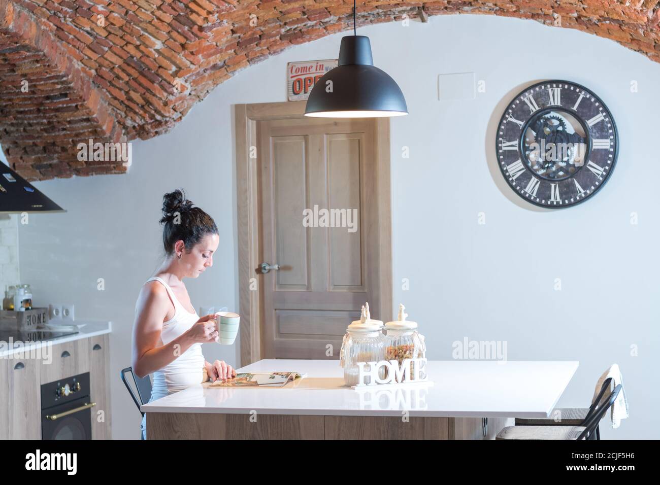 giovane bruna ragazza che legge una rivista mentre beve il caffè dentro la cucina Foto Stock