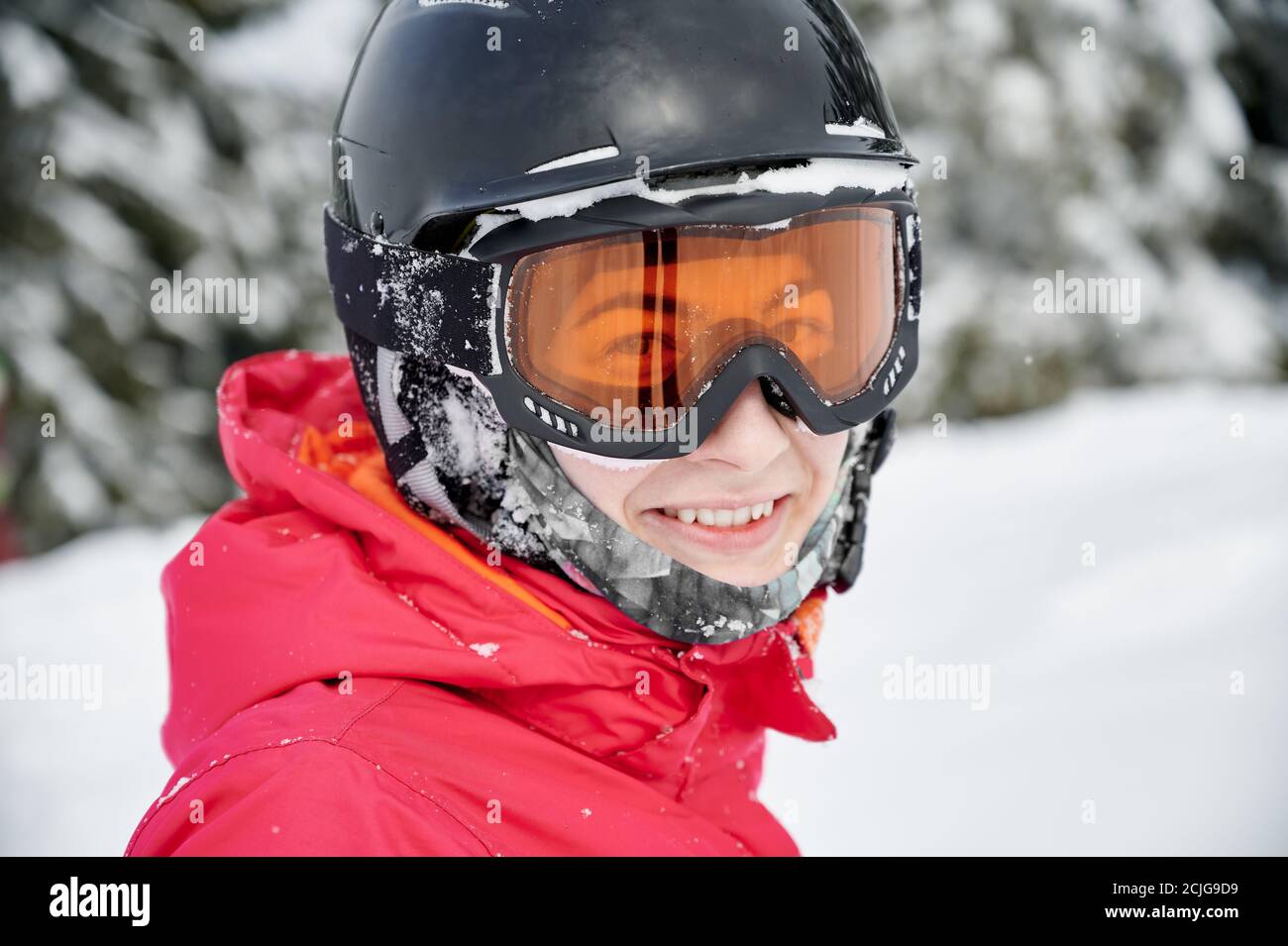 Primo piano ritratto di donna sorridente con giacca rossa, casco e occhiali di protezione che riposa in montagne innevate. Concetto di sport invernali Foto Stock