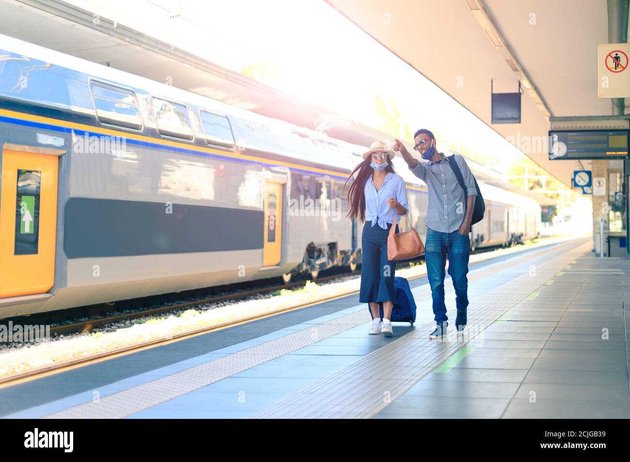 Coppia sulla piattaforma in attesa del treno - bello donna e bell'uomo in maschere mediche che camminano e hanno Viaggio durante la pandemia - nuovo normale Foto Stock