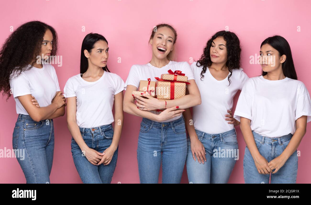 Donne invidiose guardando amico con molti regali, sfondo rosa Foto Stock