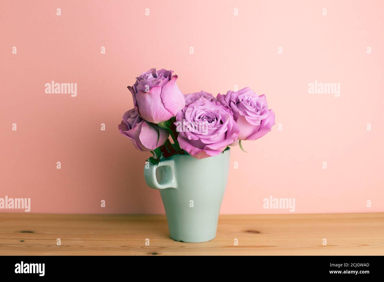 Fiori di rosa viola in tazza di ceramica su tavolo di legno con sfondo rosa. Arrangiamento floreale, spazio copia Foto Stock