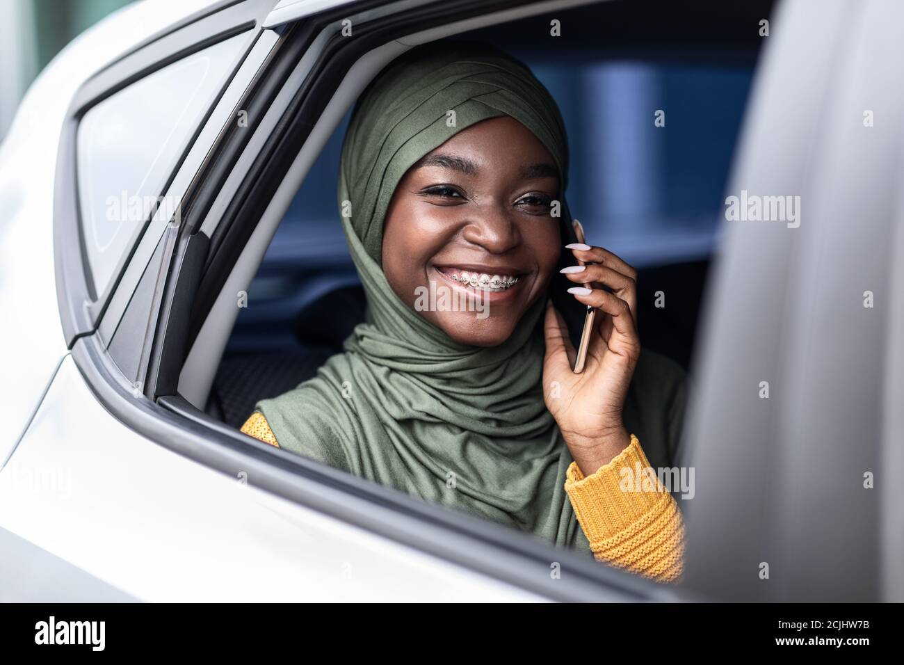 Donna musulmana nera che viaggia sul sedile posteriore dell'auto e parla sul cellulare Foto Stock