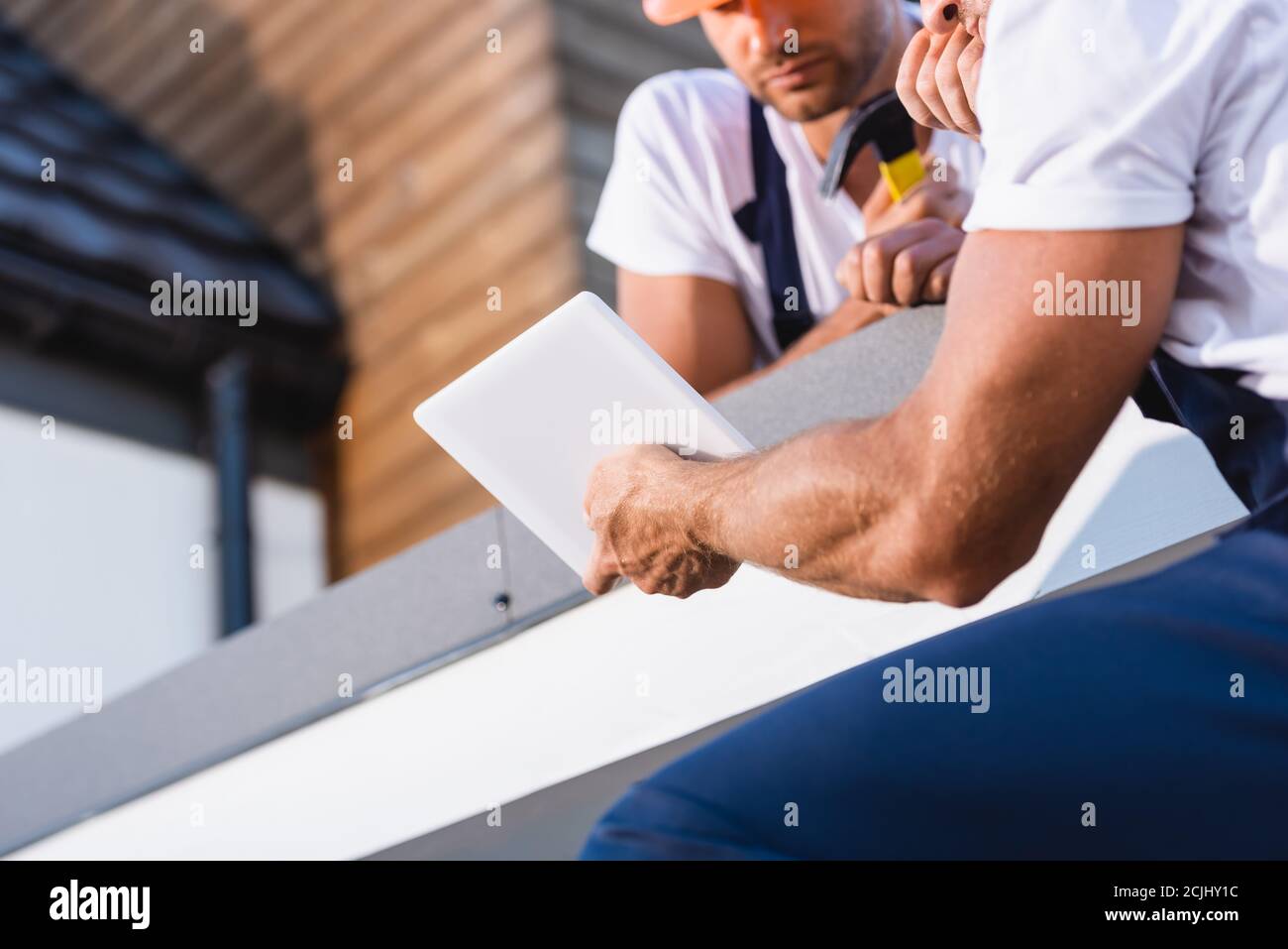 Vista ritagliata dei costruttori che utilizzano un tablet digitale sul tetto di casa Foto Stock