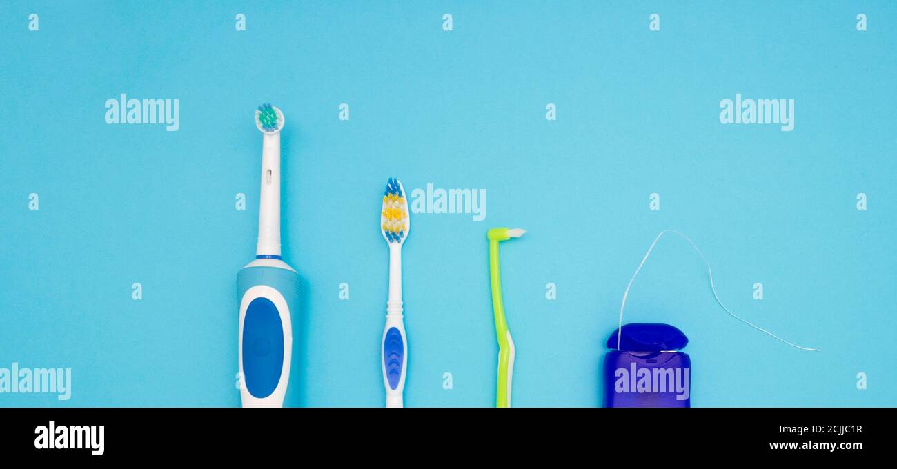 Igiene orale. Parte di uno spazzolino elettrico, spazzolini da denti e filo interdentale su sfondo blu. La vista dall'alto. Foto Stock