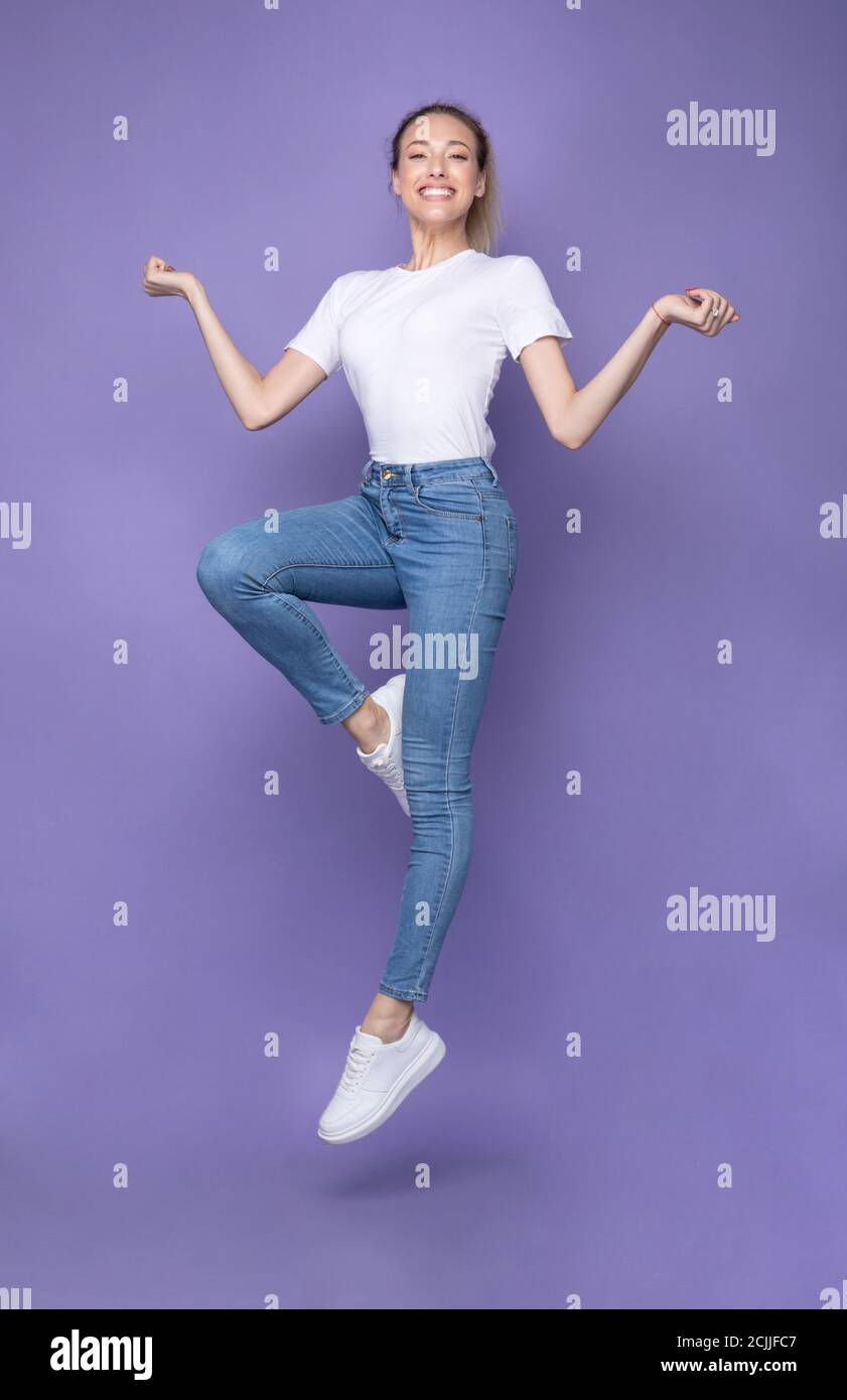 Happy Blonde Woman che saltano in posa in Mid-Air, sfondo viola, verticale Foto Stock
