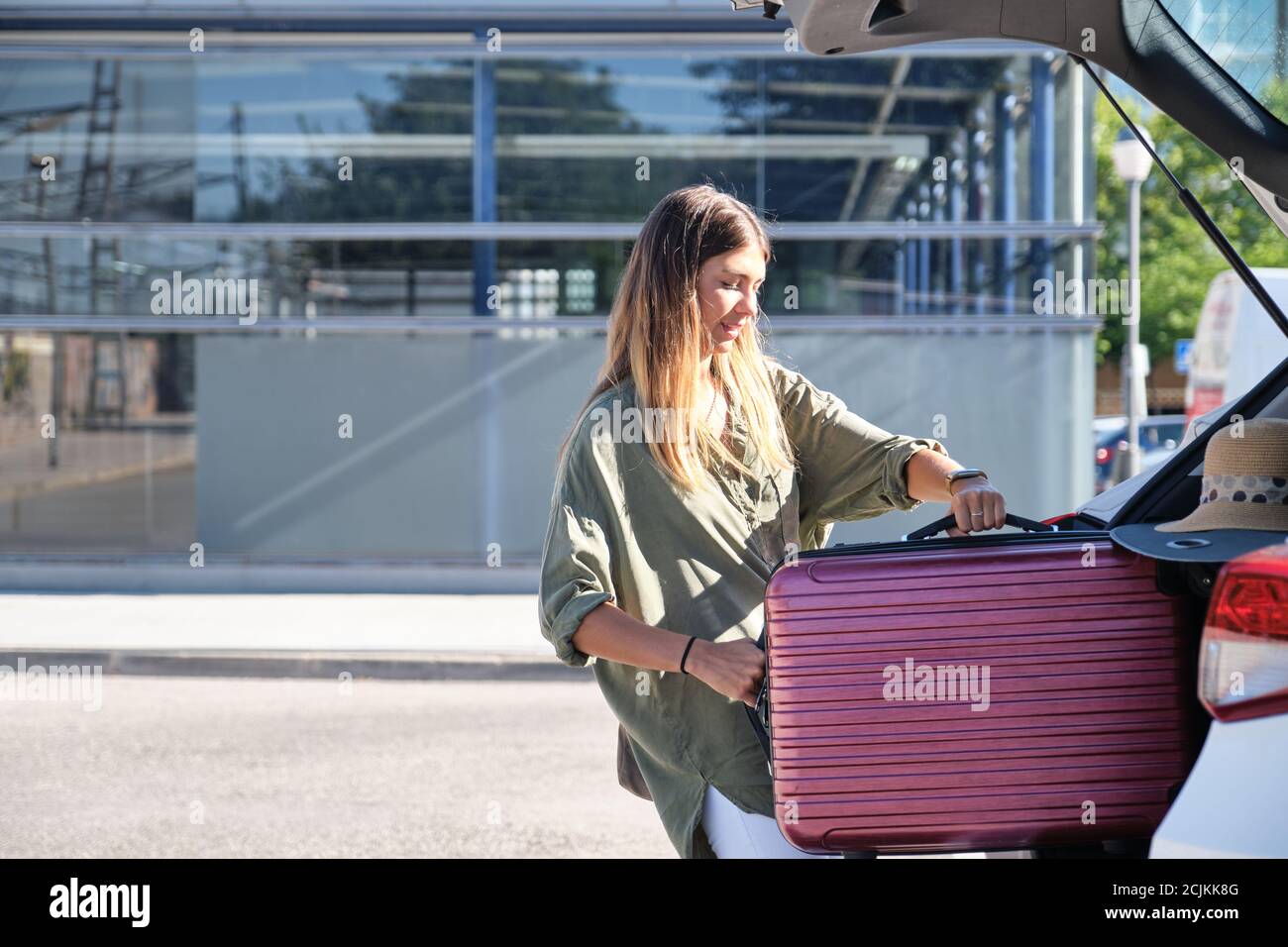 Giovane donna che inscatola la valigia nel bagagliaio dell'auto. Concetto di vacanza. Foto Stock
