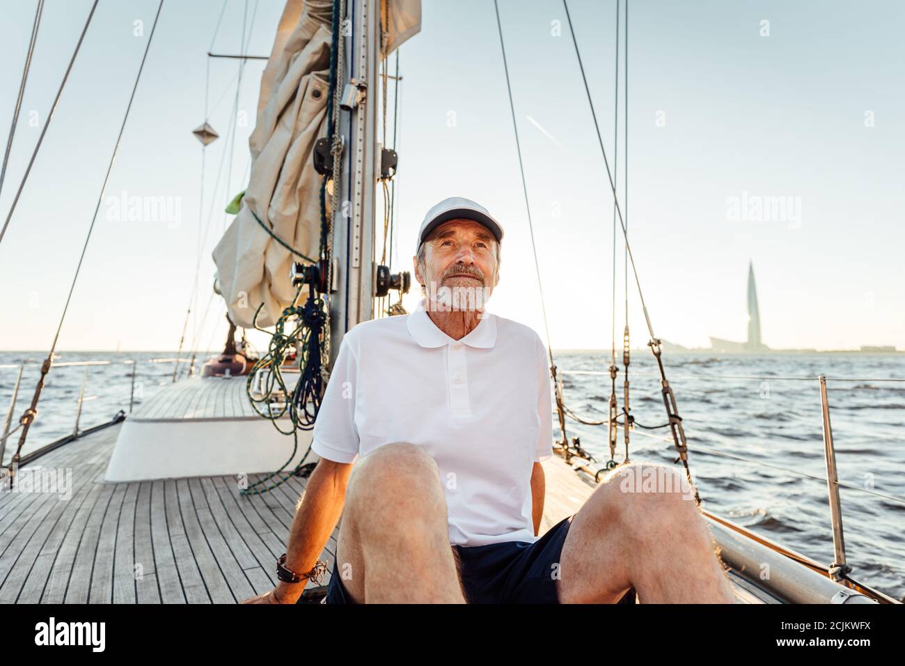 Rilassato uomo maturo seduto sul suo yacht. Yachtman riposato sulla barca al tramonto e guardando lontano. Foto Stock