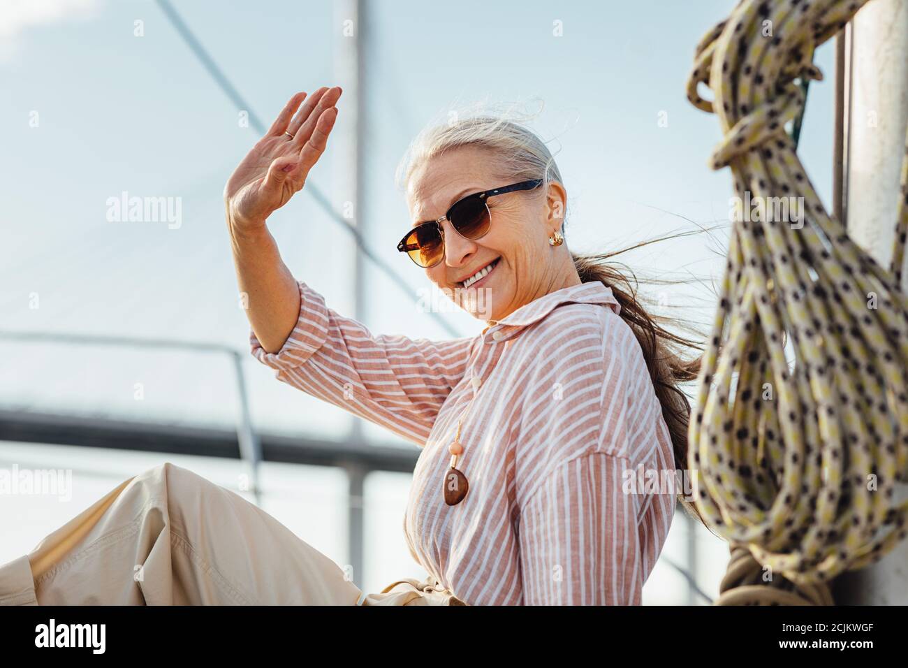 Donna felice che indossa occhiali da sole agitando la mano e guardando fotocamera Foto Stock