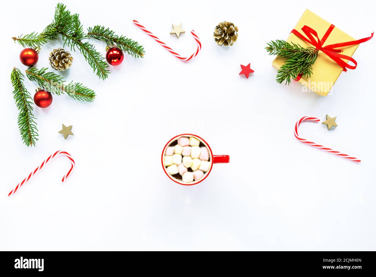 Rami di abete natalizio, caramelle rosse, coni e regalo, decorazioni e una tazza di cacao con marshmallows al centro, sfondo bianco. Vista dall'alto, disposizione piatta, c. Foto Stock
