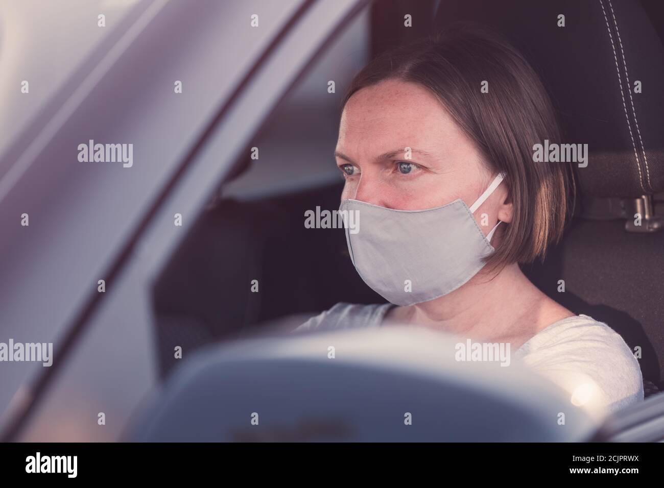 Grave conducente femminile con maschera protettiva che tiene il volante di un'auto durante le pandemie del virus corona, fuoco selettivo Foto Stock