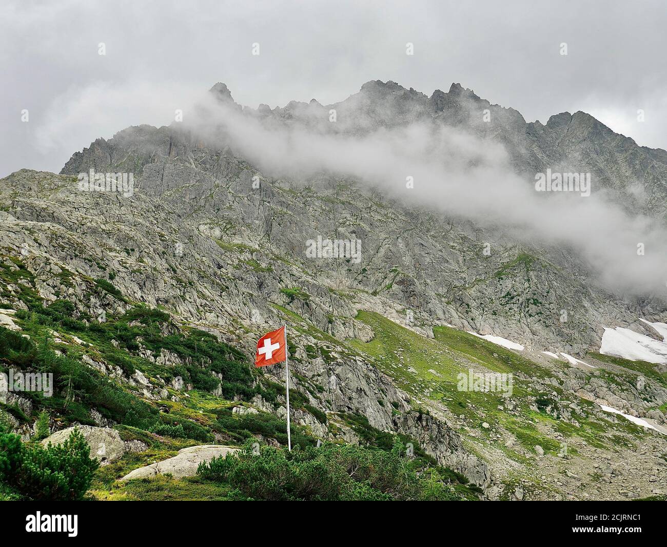 Schweizerflagge wor den wolkenbehangenen Alpen. Schöne Komposition aus Bergen, Wolken und der Schweizer Flagge. Foto Stock