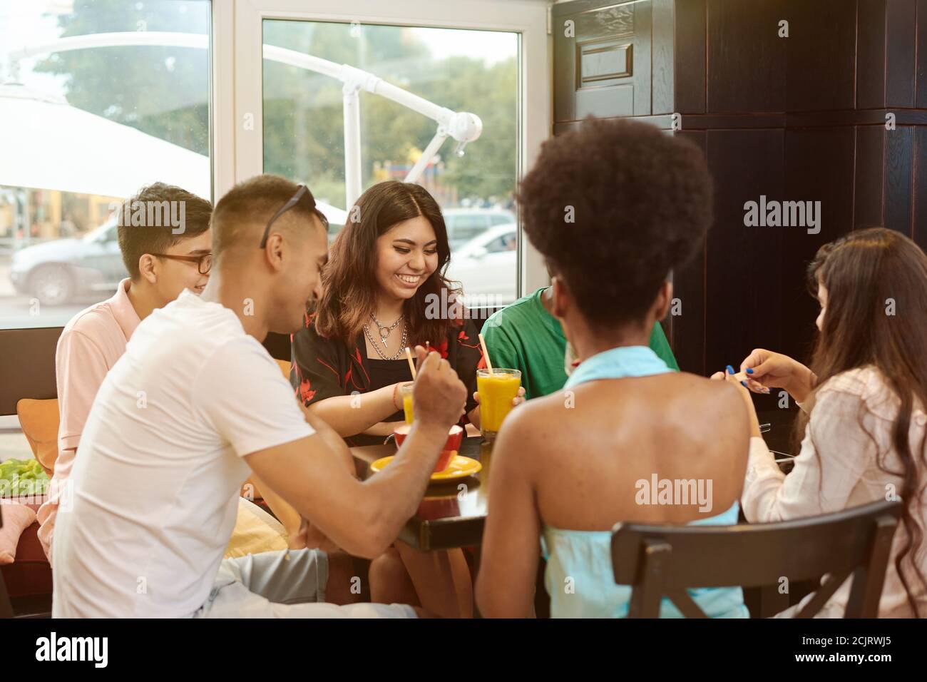 Multirazziale Happy Young drink caffè al bar, in bianco e nero allegri compagni ridere gustando bevande divertendosi seduti insieme al tavolo del ristorante, diversi amici condividono il pranzo al meeting. Foto Stock