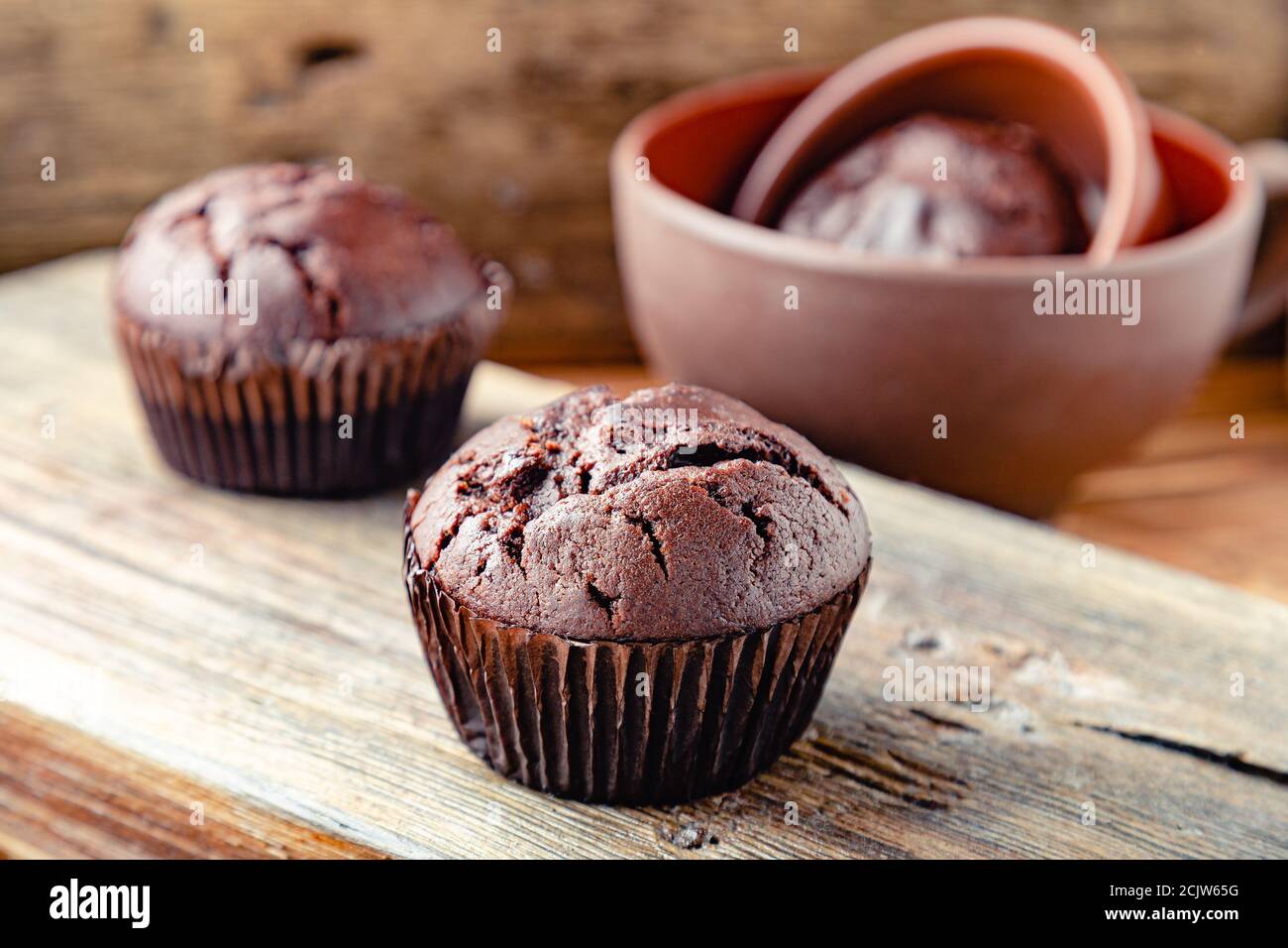 Cupcake al cioccolato sul tavolo in stile rustico. Muffin al cioccolato appena sfornati senza top su sfondo di legno scuro. Cupcake senza crema di condimento Foto Stock
