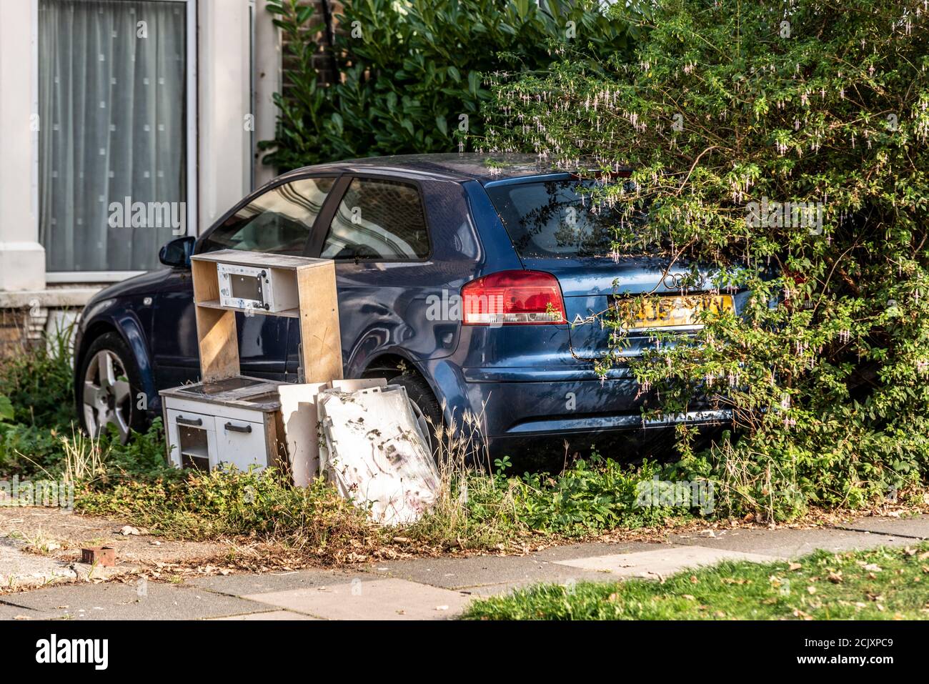 Macchina sopravsviluppata nel giardino anteriore della casa, con i rifiuti. Mobili da cucina in dumping fuori nel cortile di fronte, auto di blocco. Blu Audi A3 a sinistra per decadere nel cespuglio Foto Stock