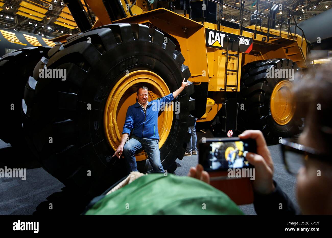 Un uomo si pone su una ruota di un escavatore Caterpillar alla fiera  "Bauma" per macchine da costruzione, macchine per materiali edili, macchine  per miniera, veicoli per l'edilizia e attrezzature per l'edilizia