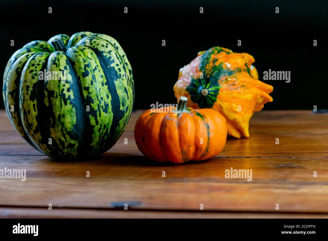 Varietà di zucche su tavola rustica in legno e fondo nero chiaro. Verdure simboliche autunnali nei colori verde, giallo e arancione. Foto Stock