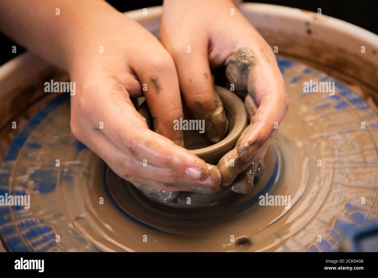Le mani del bambino che modellano una pentola su una ruota di ceramica che gira. Foto Stock