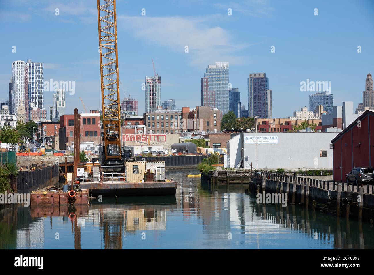 Vista del canale Gowanus a Brooklyn, NY con una chiatta e una gru da costruzione. Sullo sfondo sono i grattacieli del centro di Brooklyn. Foto Stock