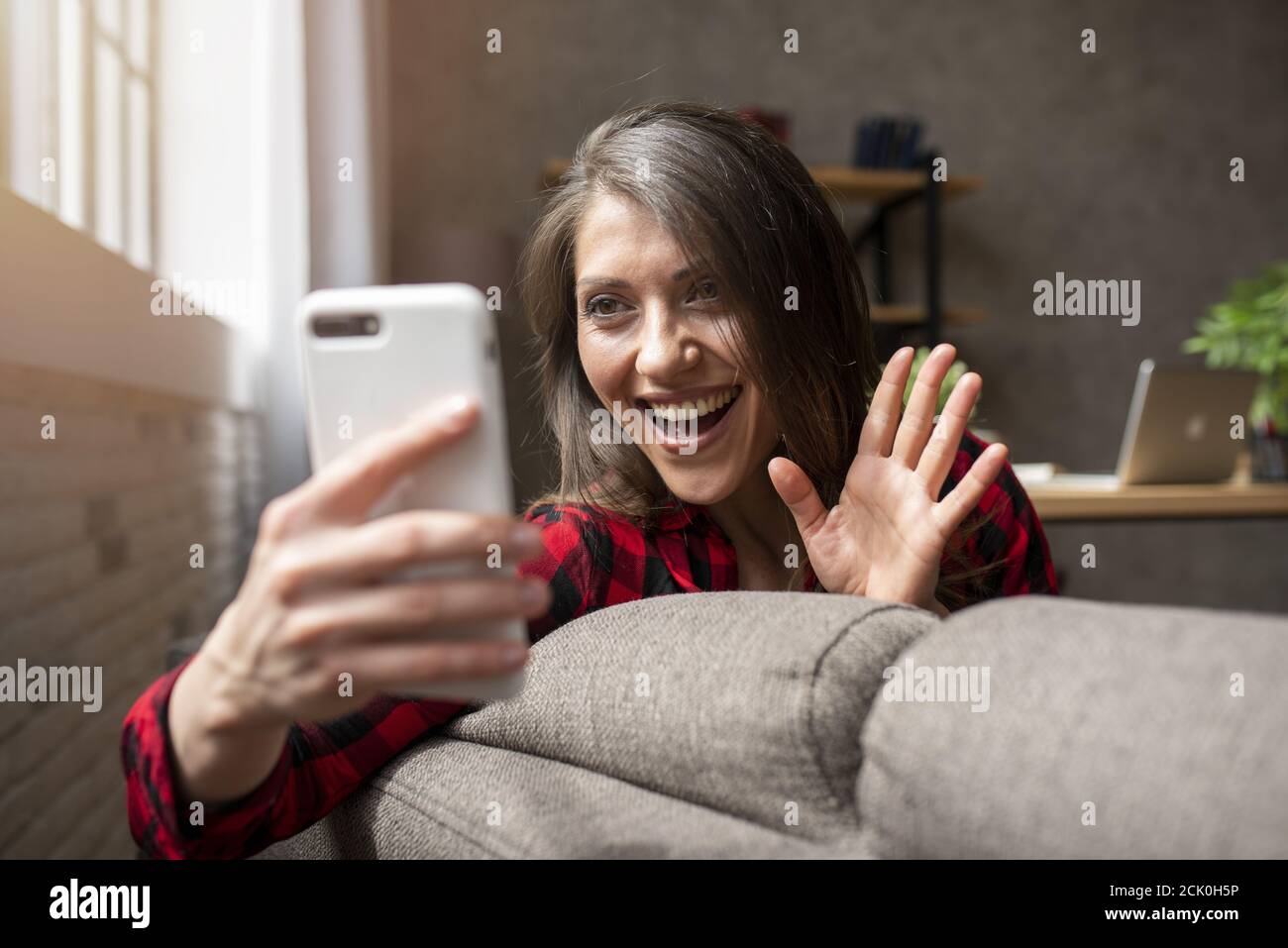 La ragazza inizia una videochiamata con il suo smartphone sul divano Foto Stock