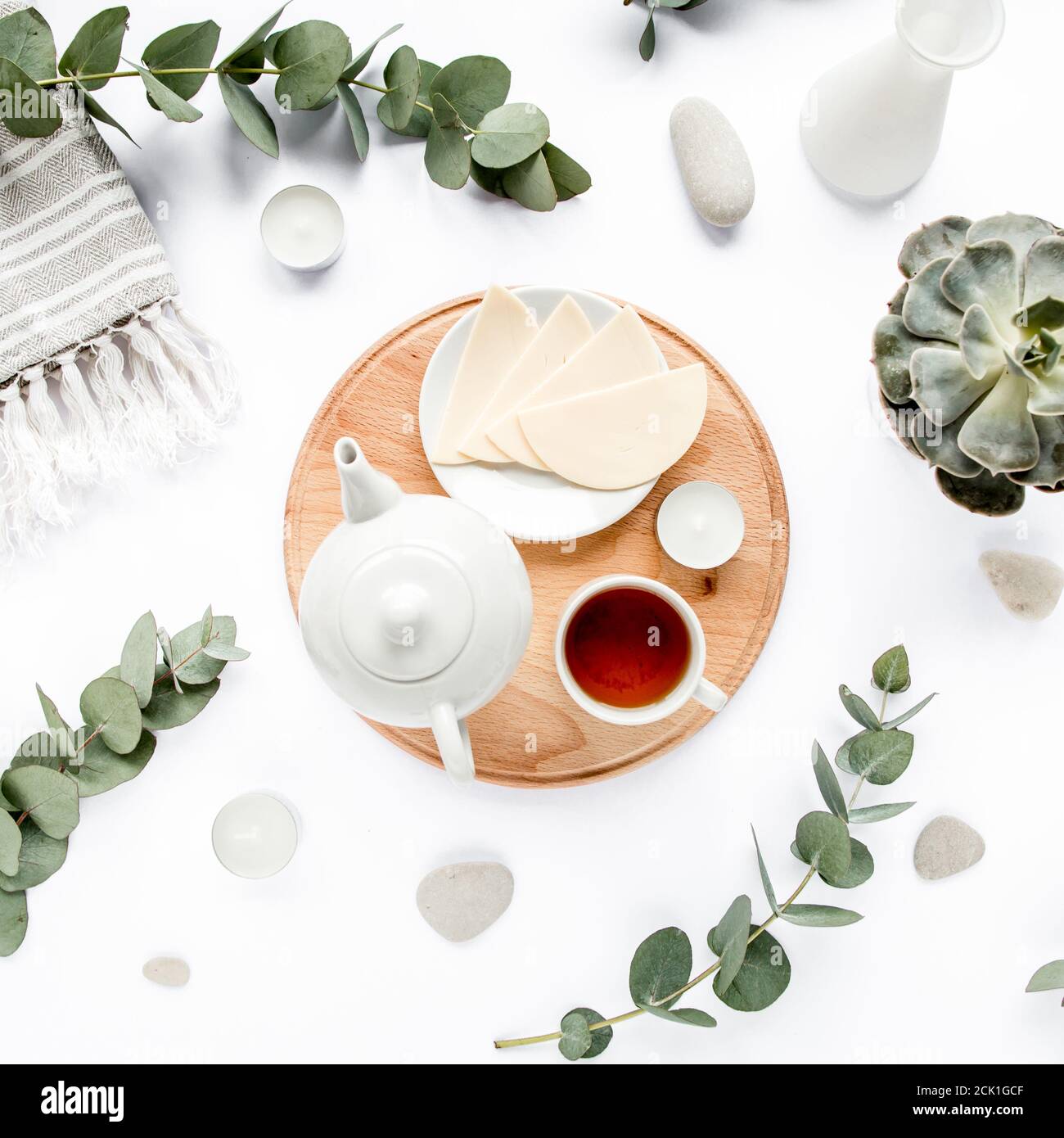 Prima colazione con formaggio, foglie di eucalipto, tagliere e tè nero composizione con su sfondo bianco. Disposizione piatta, vista dall'alto Foto Stock