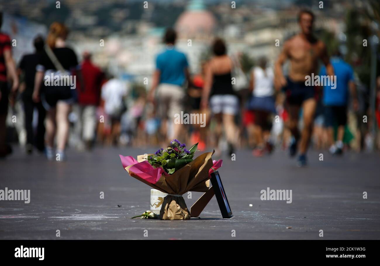 Le persone camminano vicino a un bouquet di fiori messo in omaggio alle vittime dell'attacco di camion lungo la Promenade des Anglais in Bastille Day uccidendo punteggi e ferendo come molti a Nizza, Francia, 17 luglio 2016. IMMAGINI TPX REUTERS/ERIC GAILLARD DEL GIORNO Foto Stock