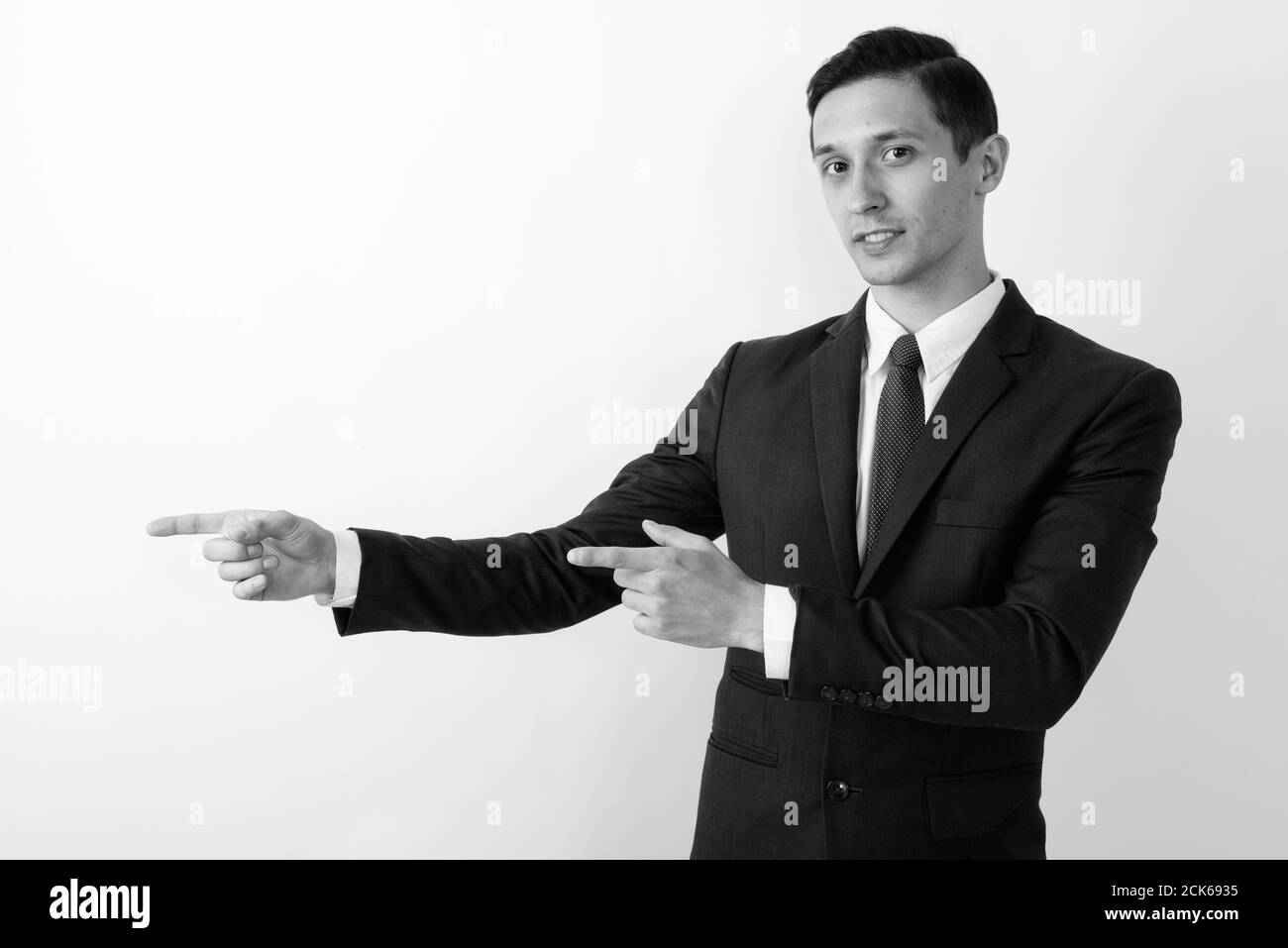 Studio di giovane bel uomo d'affari che mostra qualcosa mentre indica dita su sfondo bianco Foto Stock