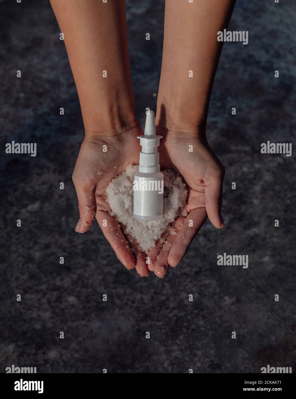 Mani con sale e una bottiglia di farmaco. Il trattamento dei raffreddori avviene tramite spray nasale Foto Stock