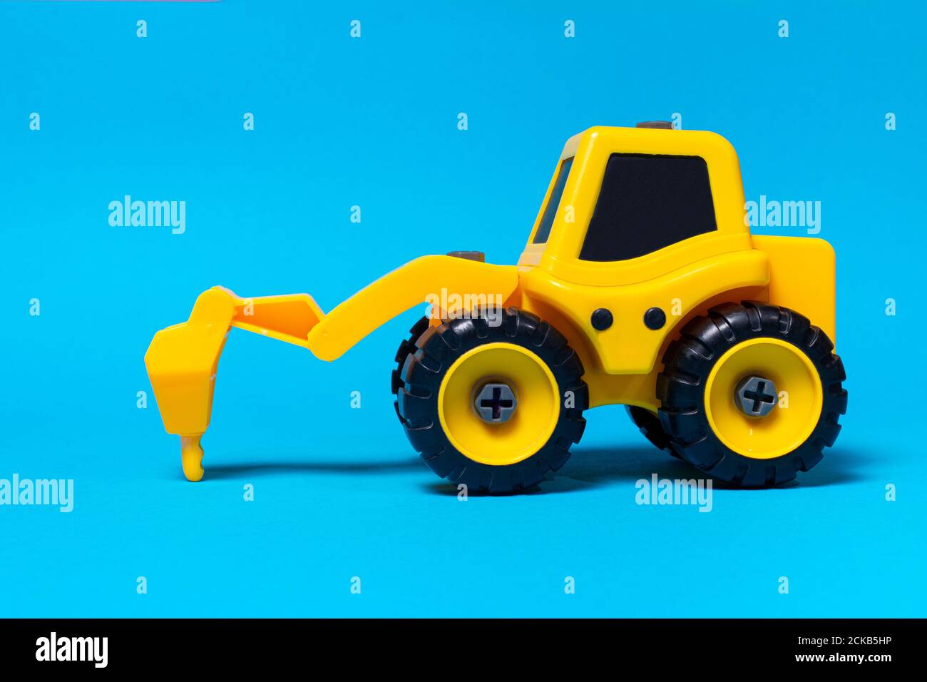 Trattore giallo giocattolo per bambini su fondo blu. Attrezzature di costruzione in plastica, negozio di giocattoli Foto Stock