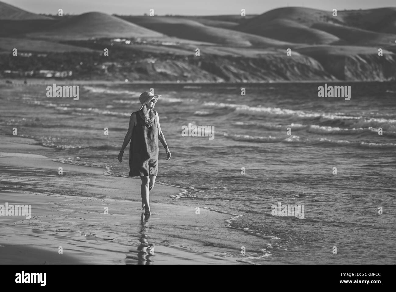Felice attraente donna matura in abito rosso godendo di camminare all'aperto e la libertà sulla spiaggia con l'oceano blu e bellissimo paesaggio. Viaggi, persone, Foto Stock