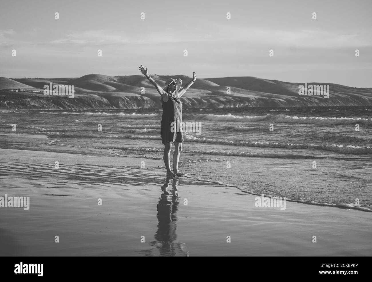 Felice attraente donna matura in abito rosso godendo all'aperto e la libertà sulla spiaggia, braccia aperte con oceano blu e bellissimo paesaggio. Foto Stock