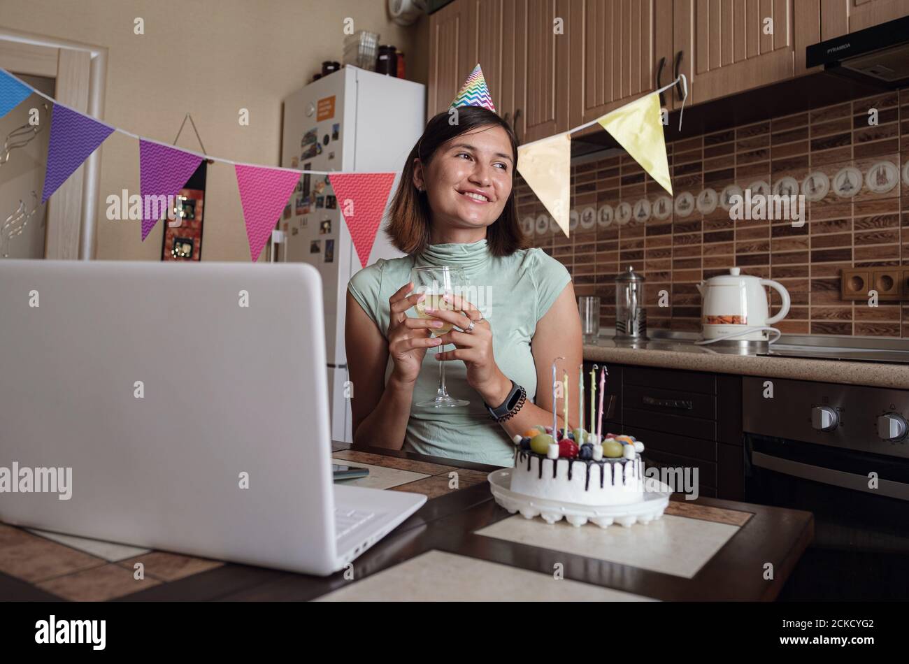 Ragazza che festeggia il compleanno on-line nel tempo di quarantena. Fare un desiderio e soffiare le candele sulla torta. Foto Stock