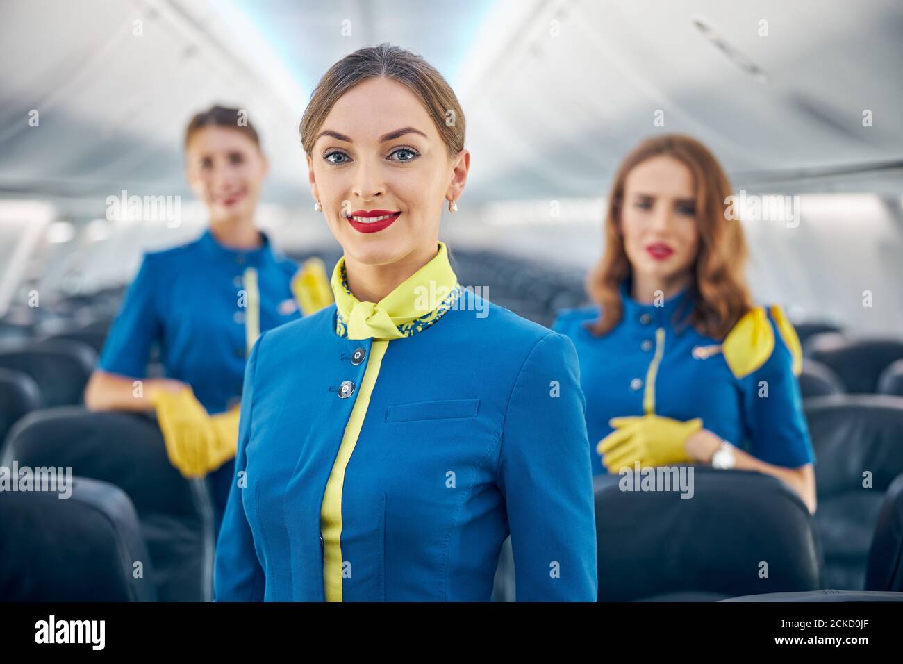Primo piano ritratto di donna allegra con uniforme blu stewards in piedi nel salone di prima classe di aereo commerciale Foto Stock