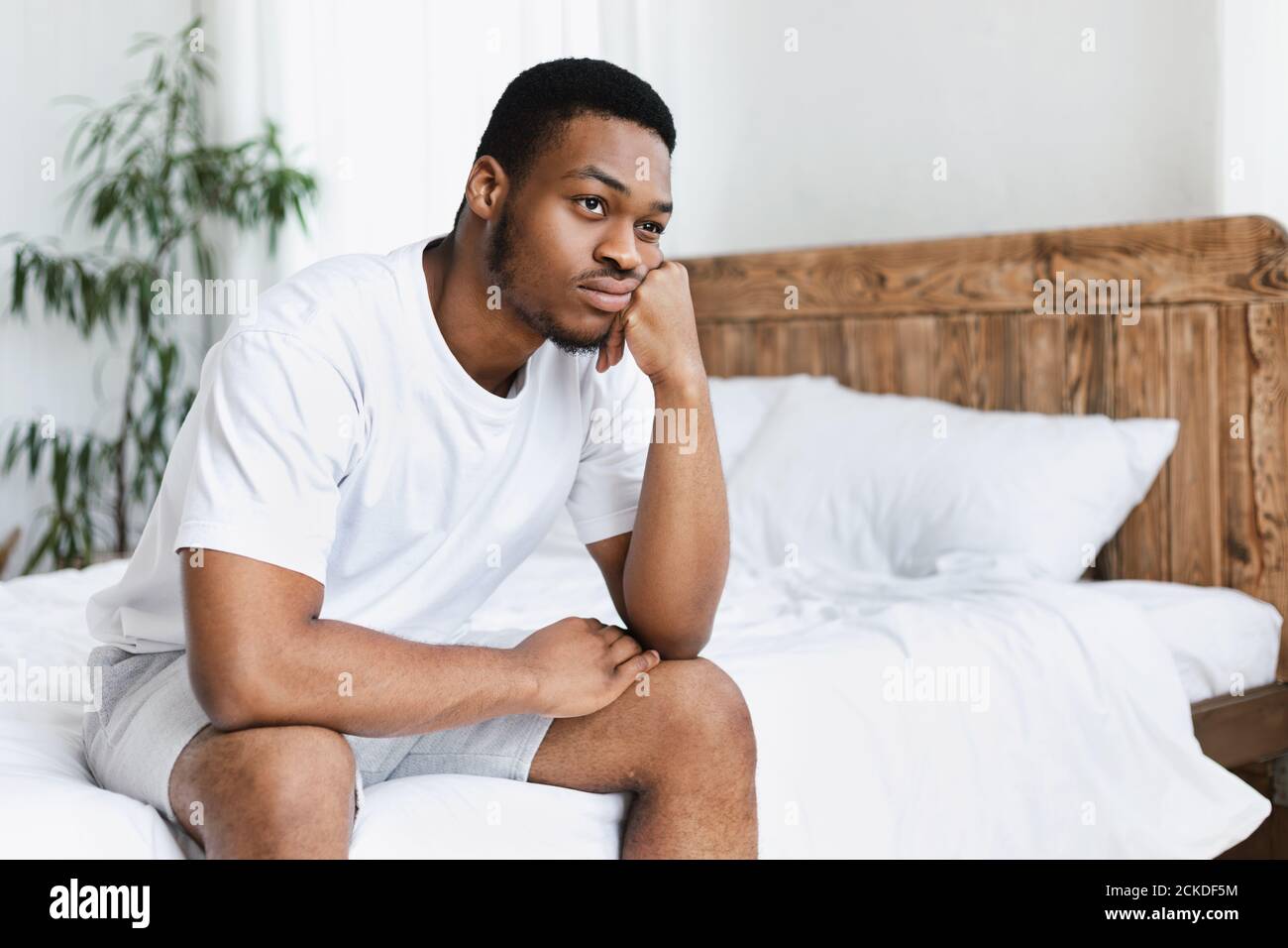 Guy nero infelice seduto sul letto in camera da letto a casa Foto Stock