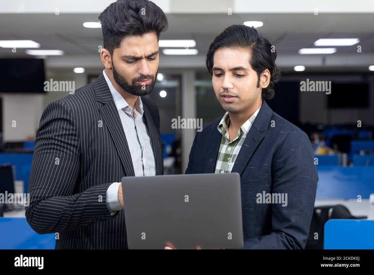 Ritratto di due giovani bei imprenditori indiani che guardano il laptop, videoconferenza con il cliente, discutere progetto, ambiente aziendale. Foto Stock